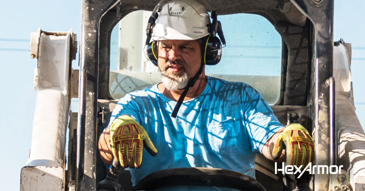 Man operating an excavator wearing a helmet, ear protection and safety gloves.