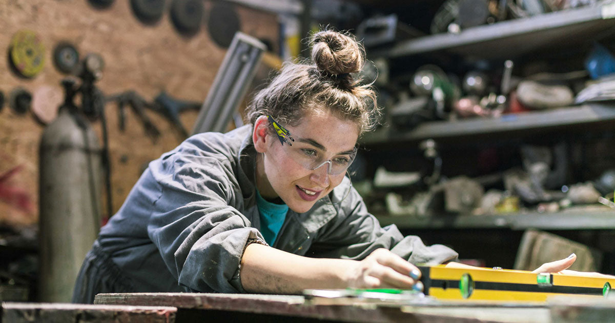 A woman in a workshop, using a level, wearing MX200S slim-fit safety glasses.